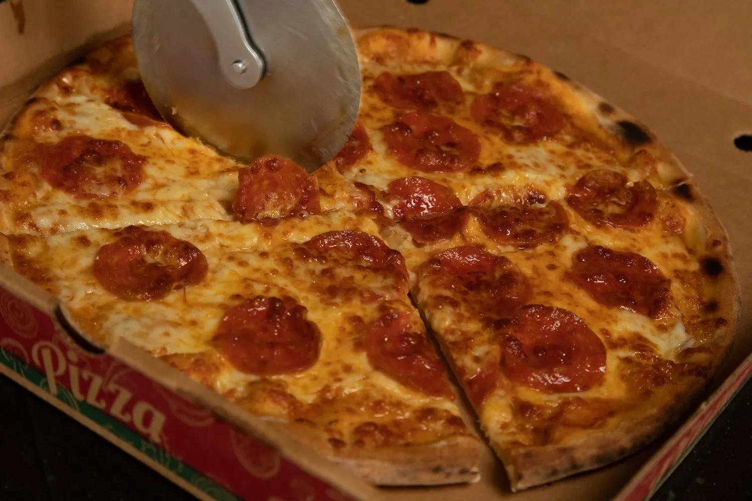 Persona corta una pizza mientras está en su caja