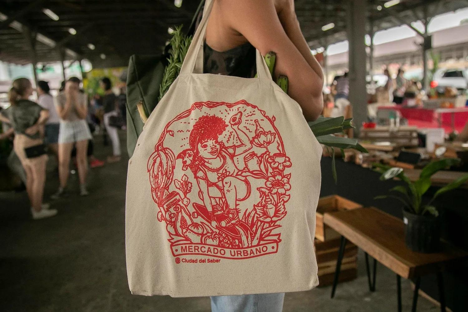Mujer sostiene en su hombre una bolsa con el logo de Mercado urbano de Ciudad del Saber